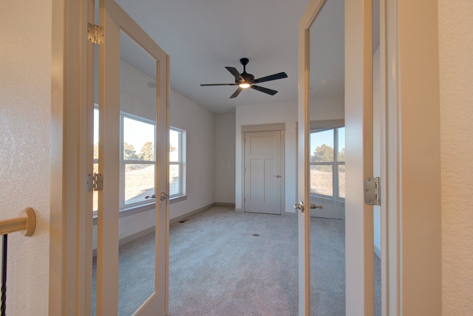 An empty room with a ceiling fan and glass doors.