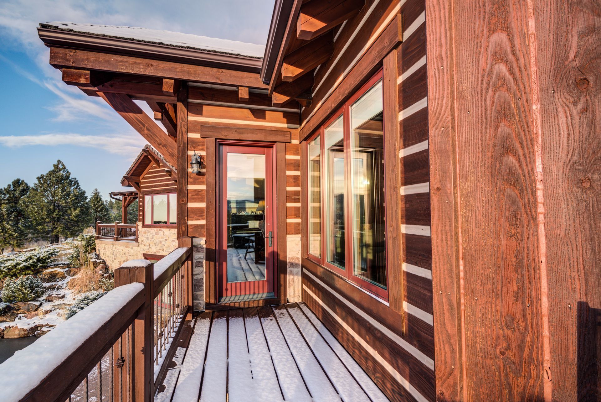 A stained wooden house with a snowy deck and a sliding glass door.