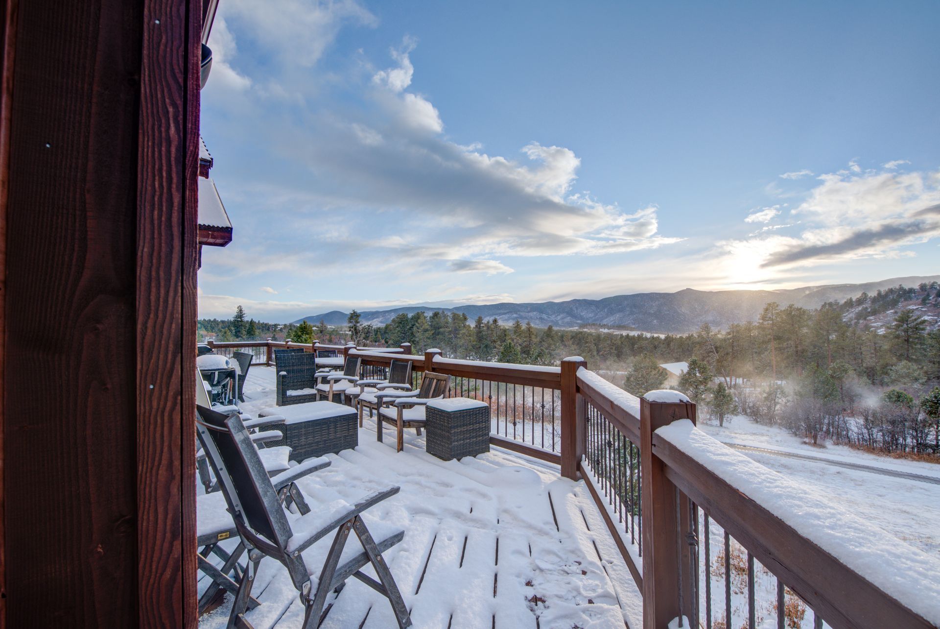 A snowy deck with chairs and a view of the mountains.