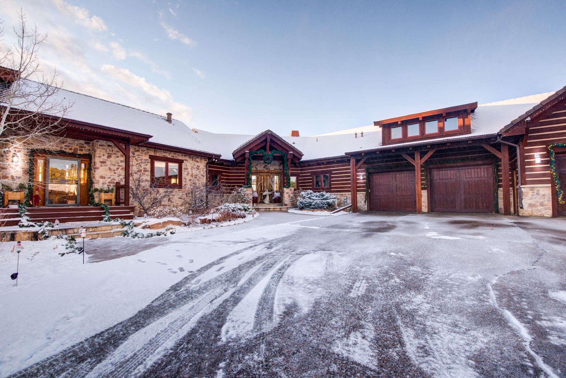 A large log style home with a snowy driveway in front of it.