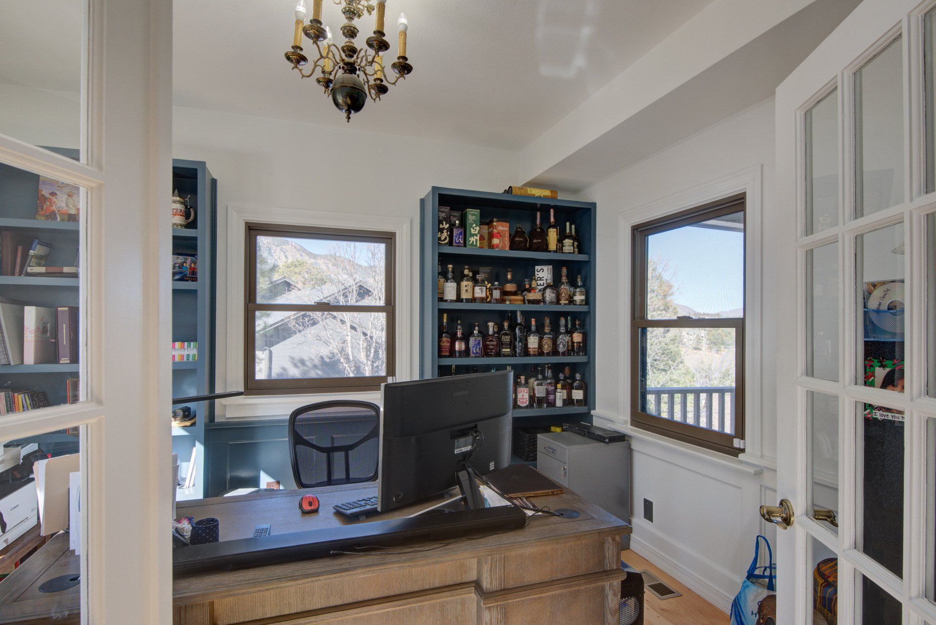 A home office with a desk , chair , computer and shelves filled with bottles of alcohol.