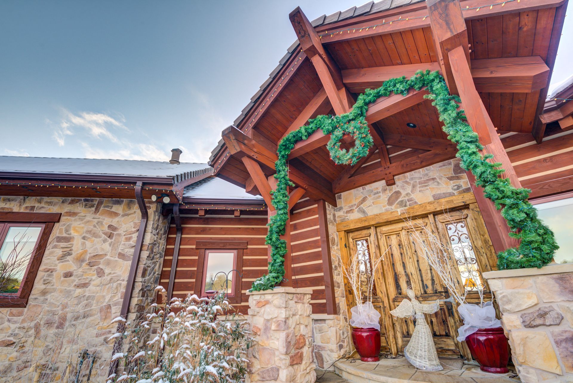 The front of a log cabin decorated for christmas with a wreath on the roof.