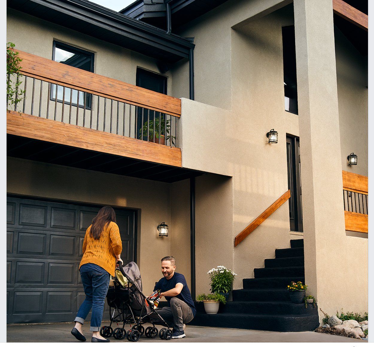A man sits on the steps of a house while a woman pushes a stroller