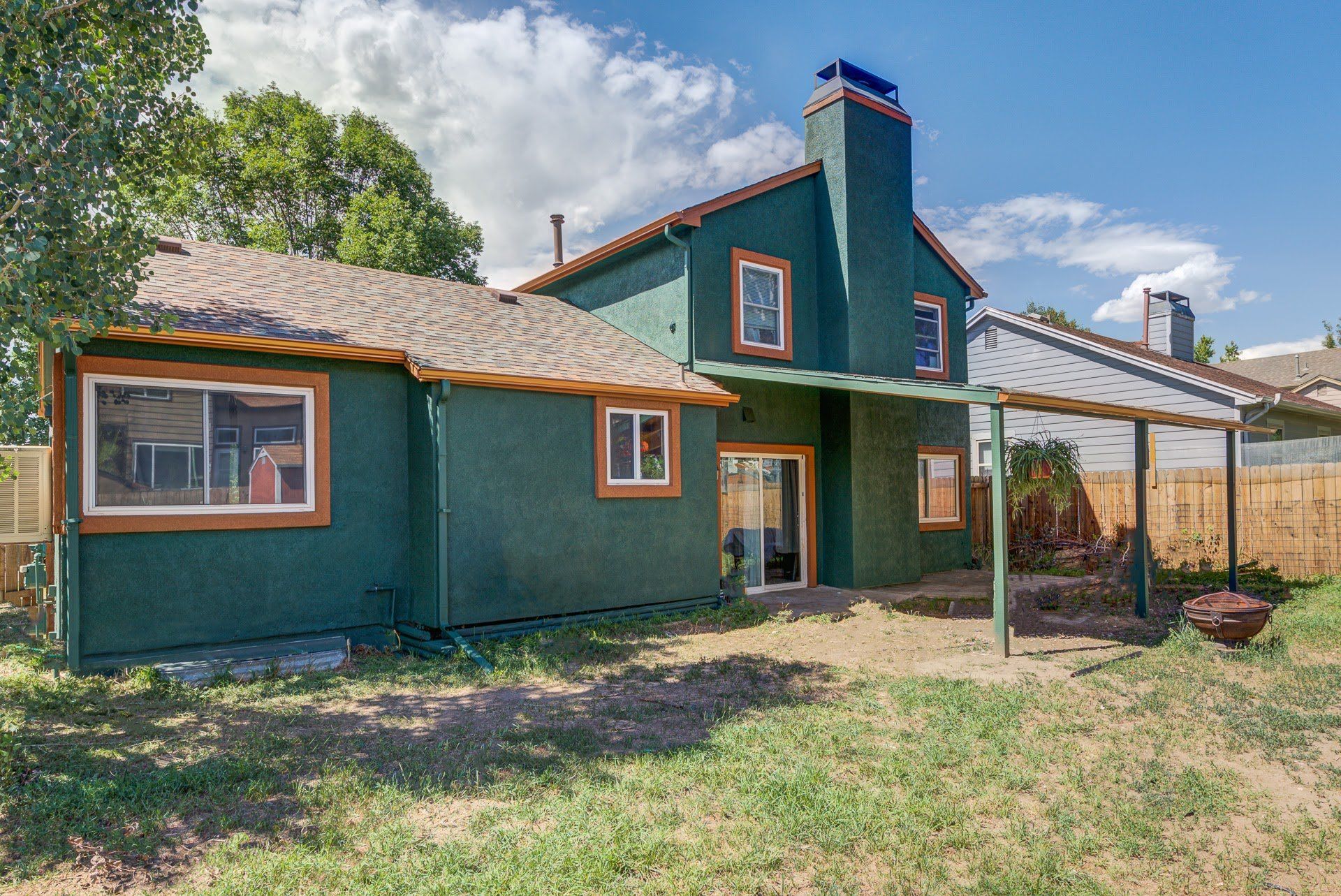 A green house with a covered patio in the backyard.