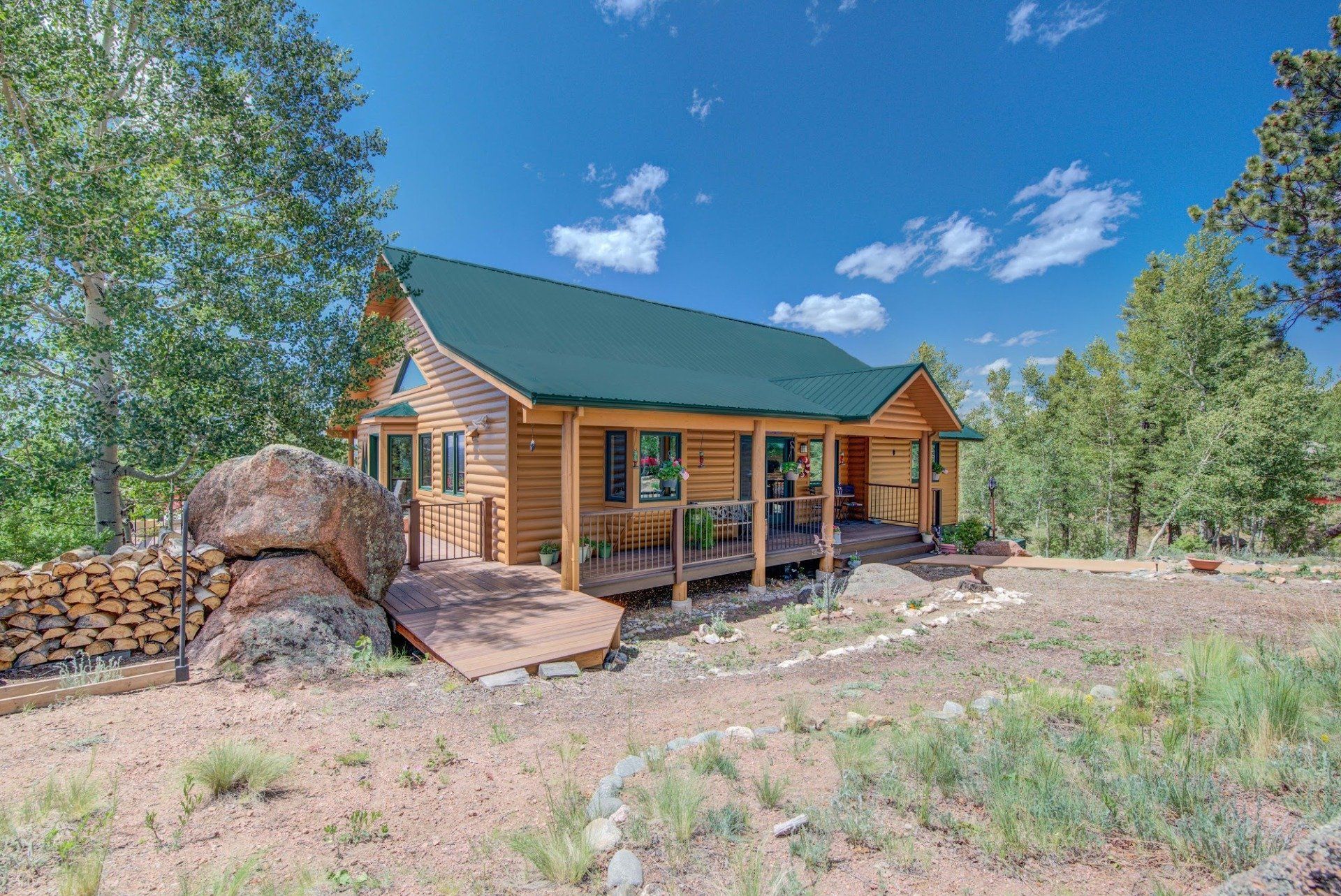 A log cabin with a green roof and a porch in the middle of a field.