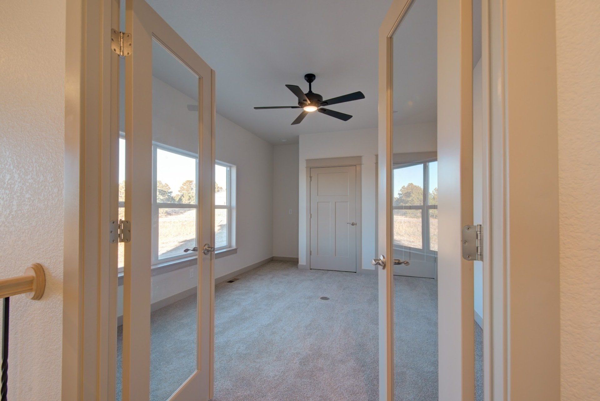 An empty room with a ceiling fan and sliding glass doors.