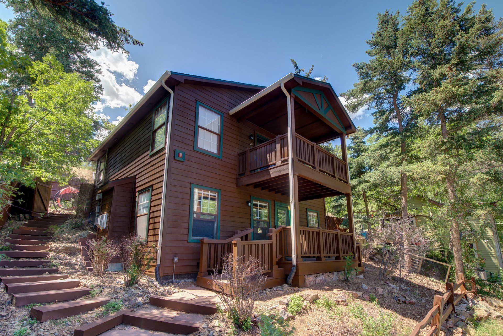 A large wooden house with stairs leading up to it is surrounded by trees.