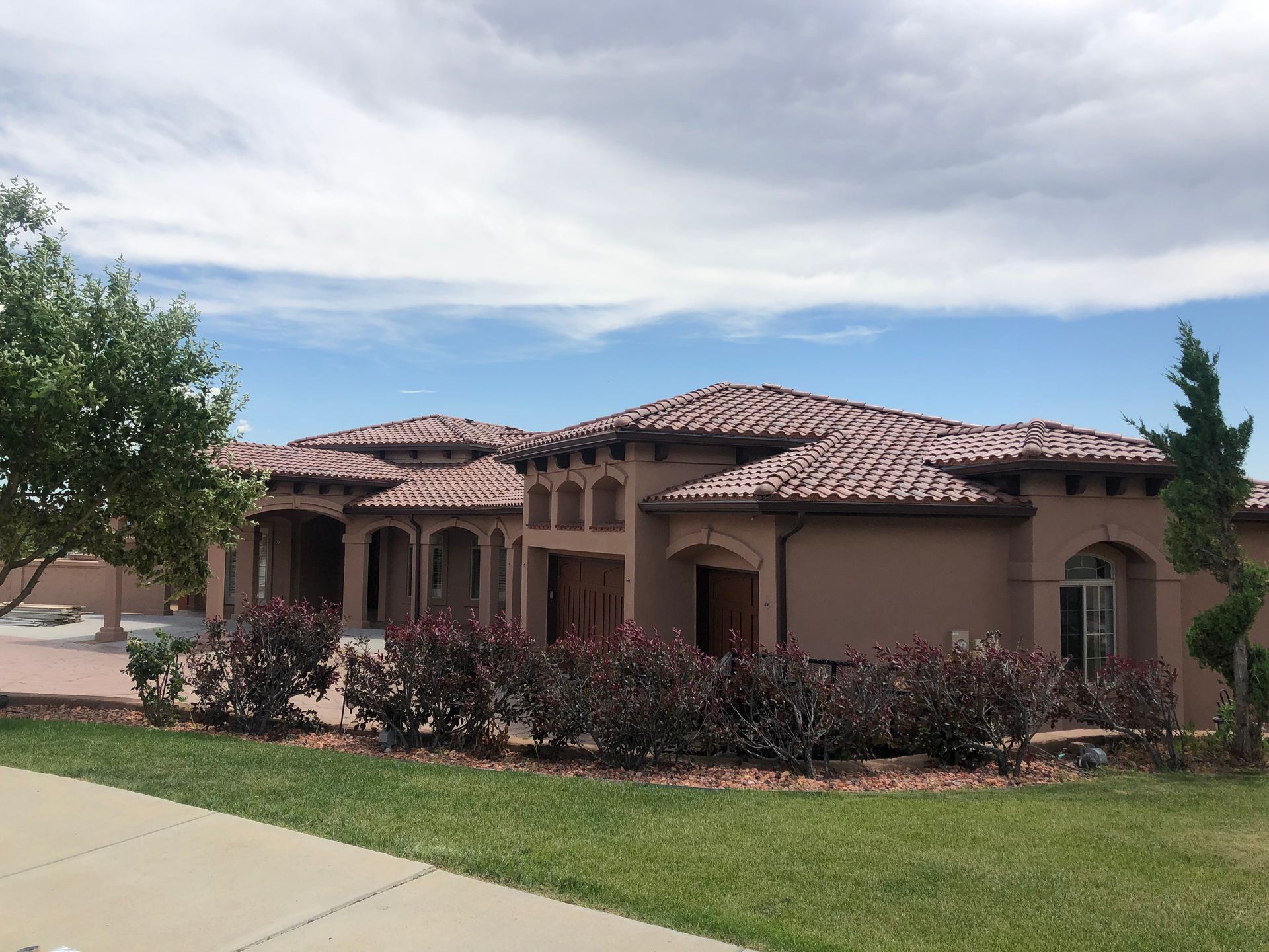 A large stucco house with a tile roof is sitting on top of a lush green lawn.