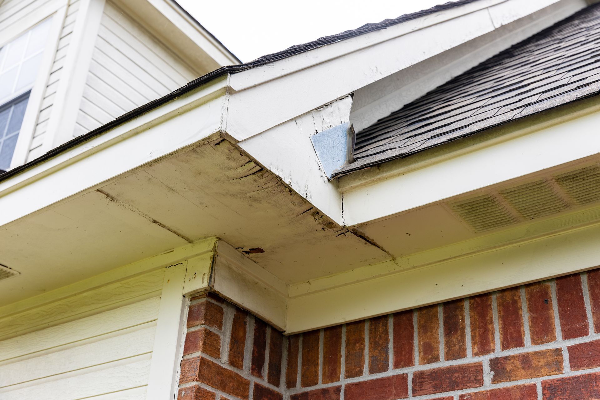 A brick house with a white roof and a white gutter showing rotten fascia and soffit wood.