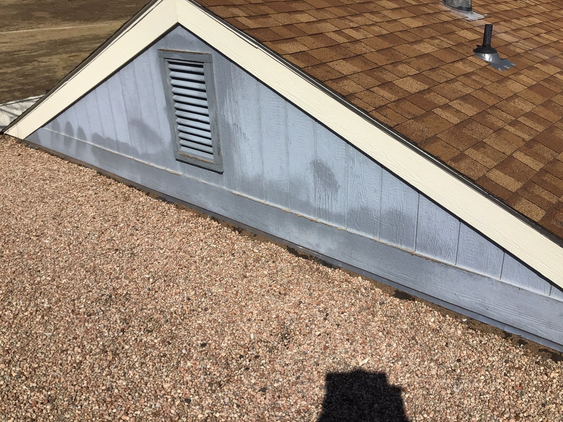 A roof with a vent on it and a shadow of a person on the ground.
