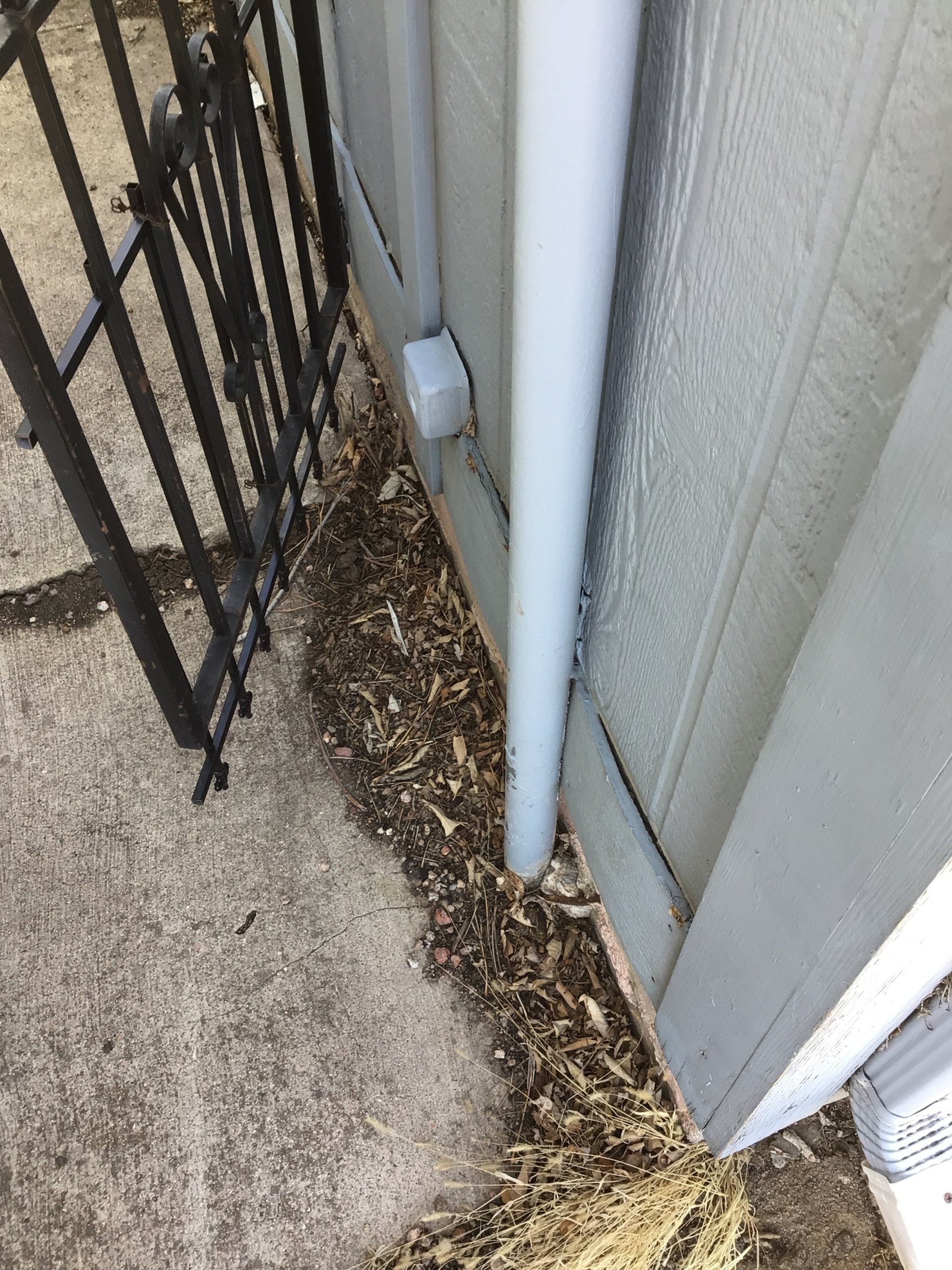 A white pipe is sitting on the side of a building next to a gate.