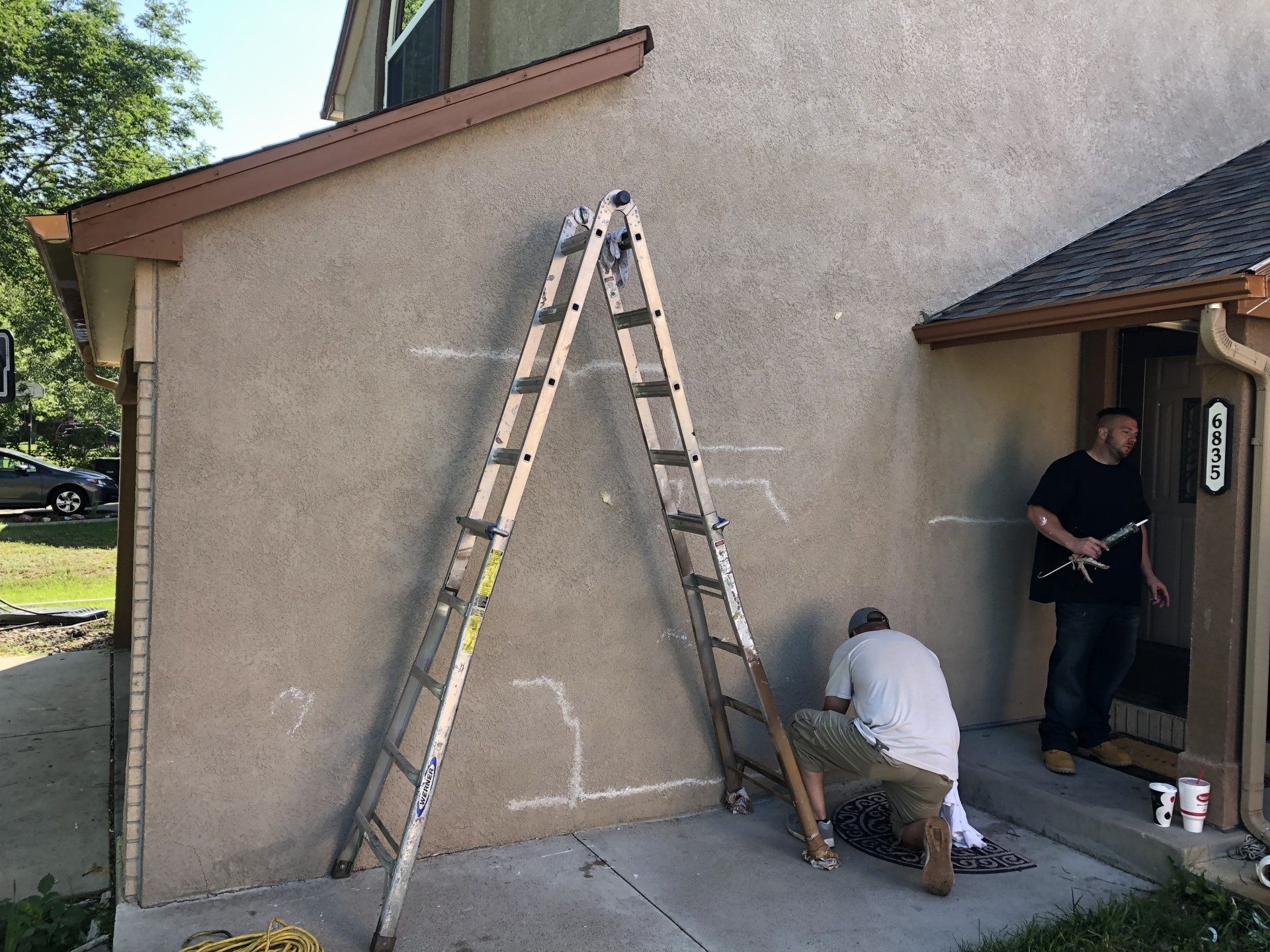 Two men are working on the side of a house with a ladder.