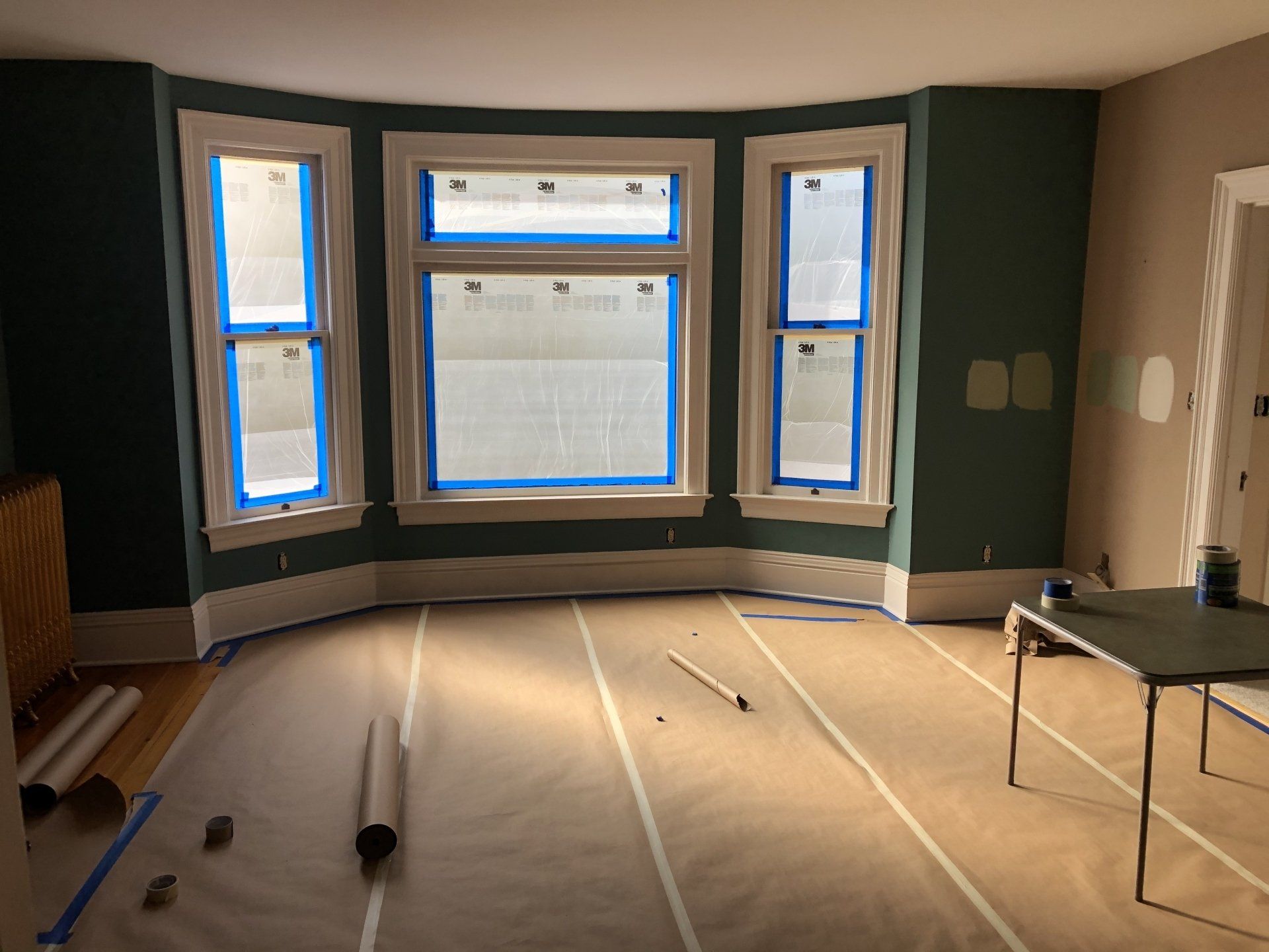 A room is being painted with blue tape on the windows.