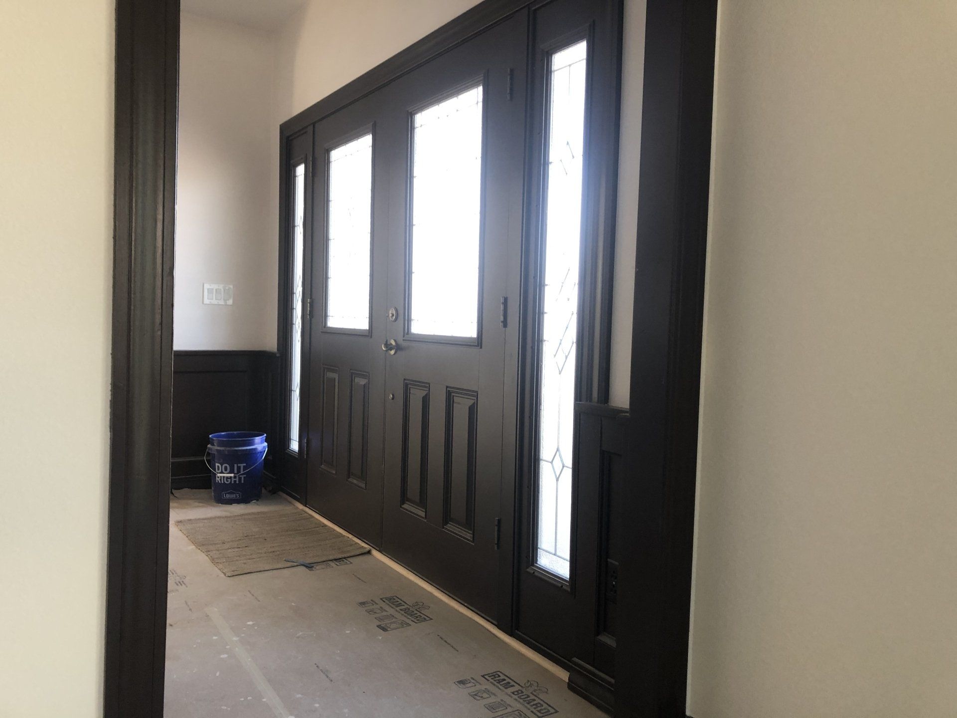 A hallway with a black door and a blue bucket on the floor.
