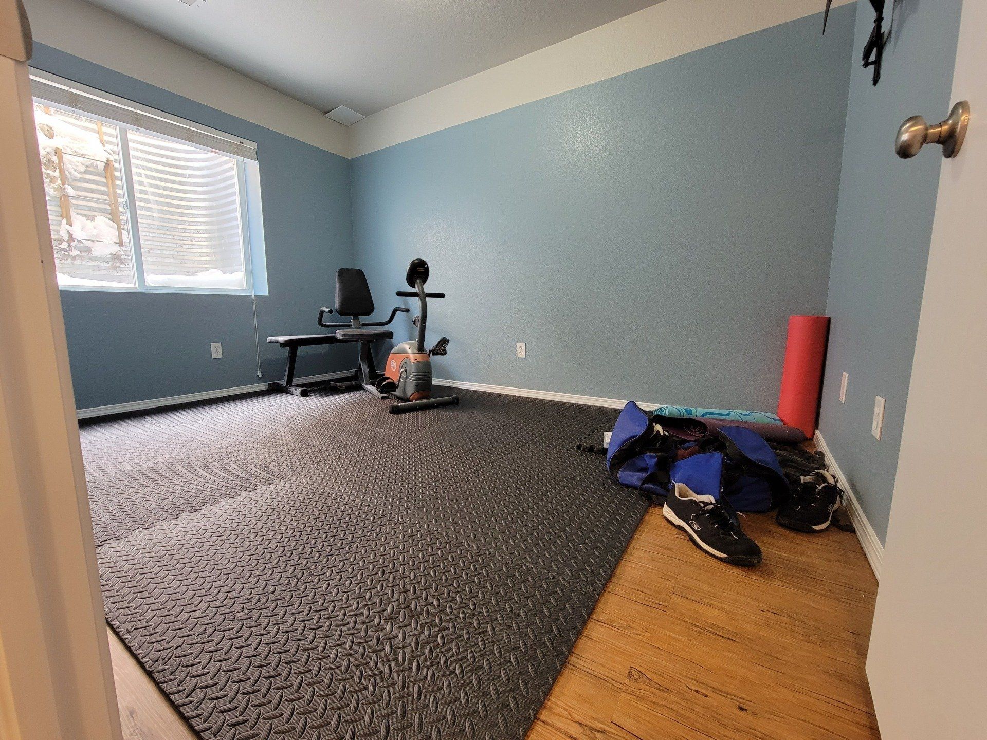 A room with a carpeted floor , a exercise bike , and a window.