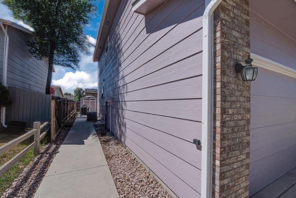 A sidewalk leading to a purple house with a brick wall