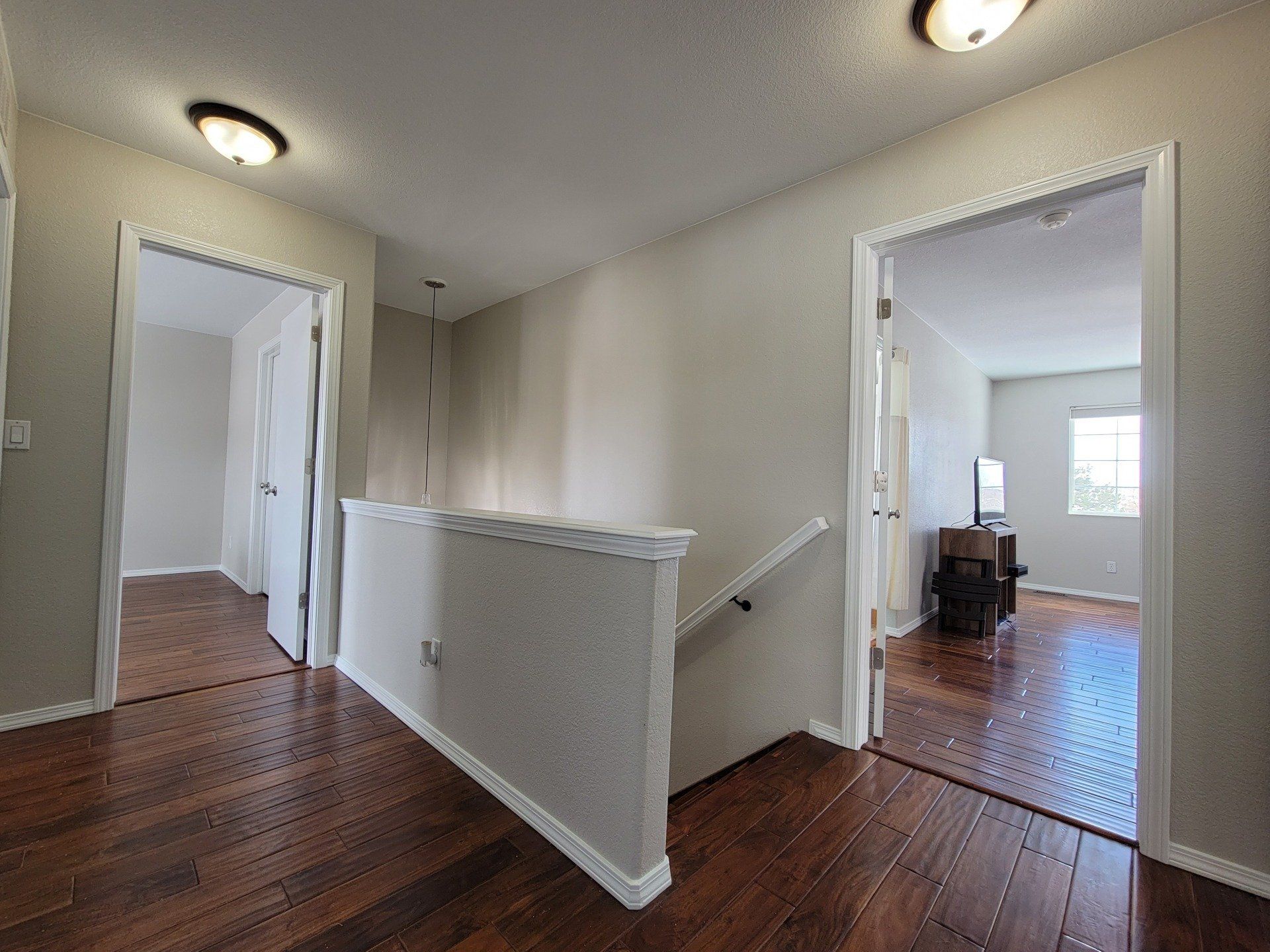 A hallway with hardwood floors and stairs leading to a living room.