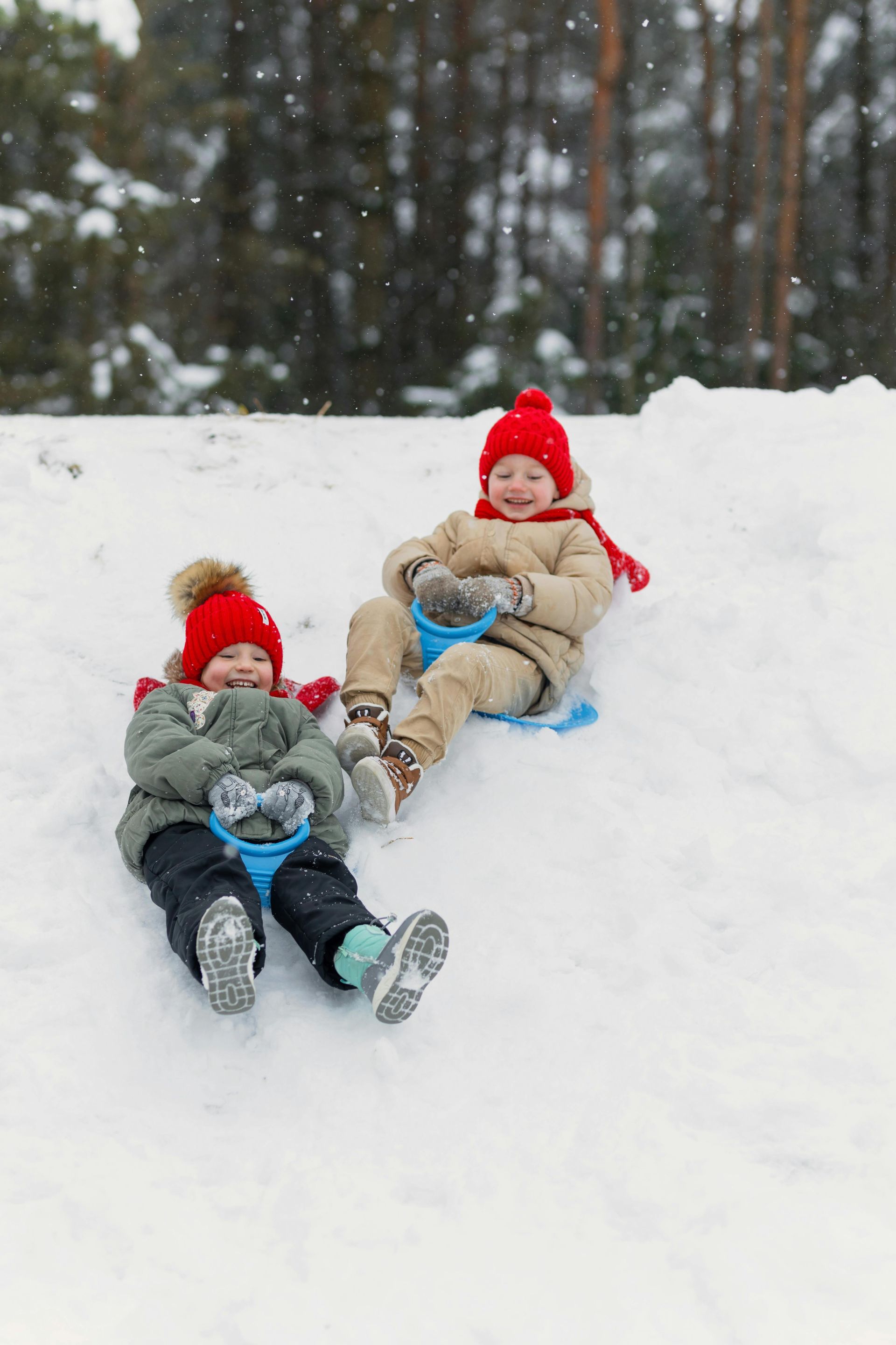 Two children are sledding down a snow covered hill.