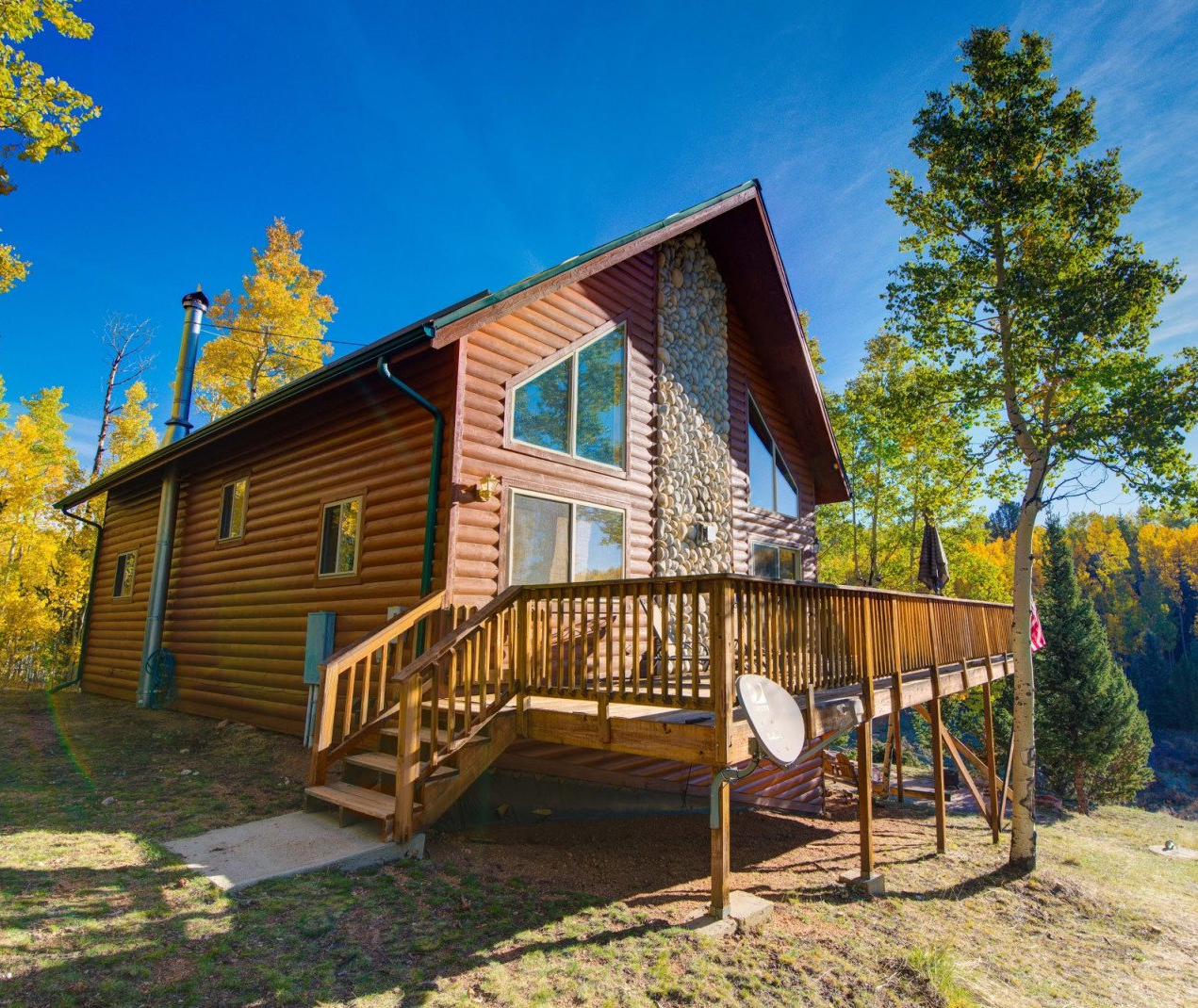A log cabin with a large deck in the middle of a forest.
