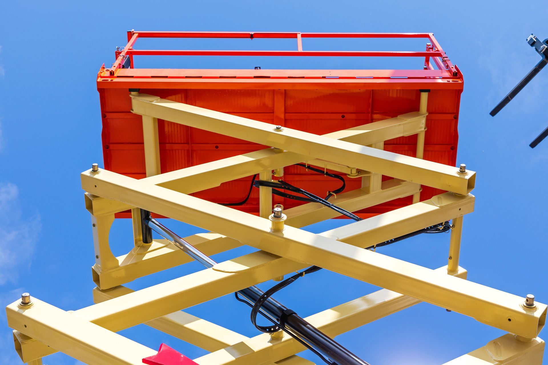 Close-up view of a yellow scissor lift with an orange platform against a clear blue sky.