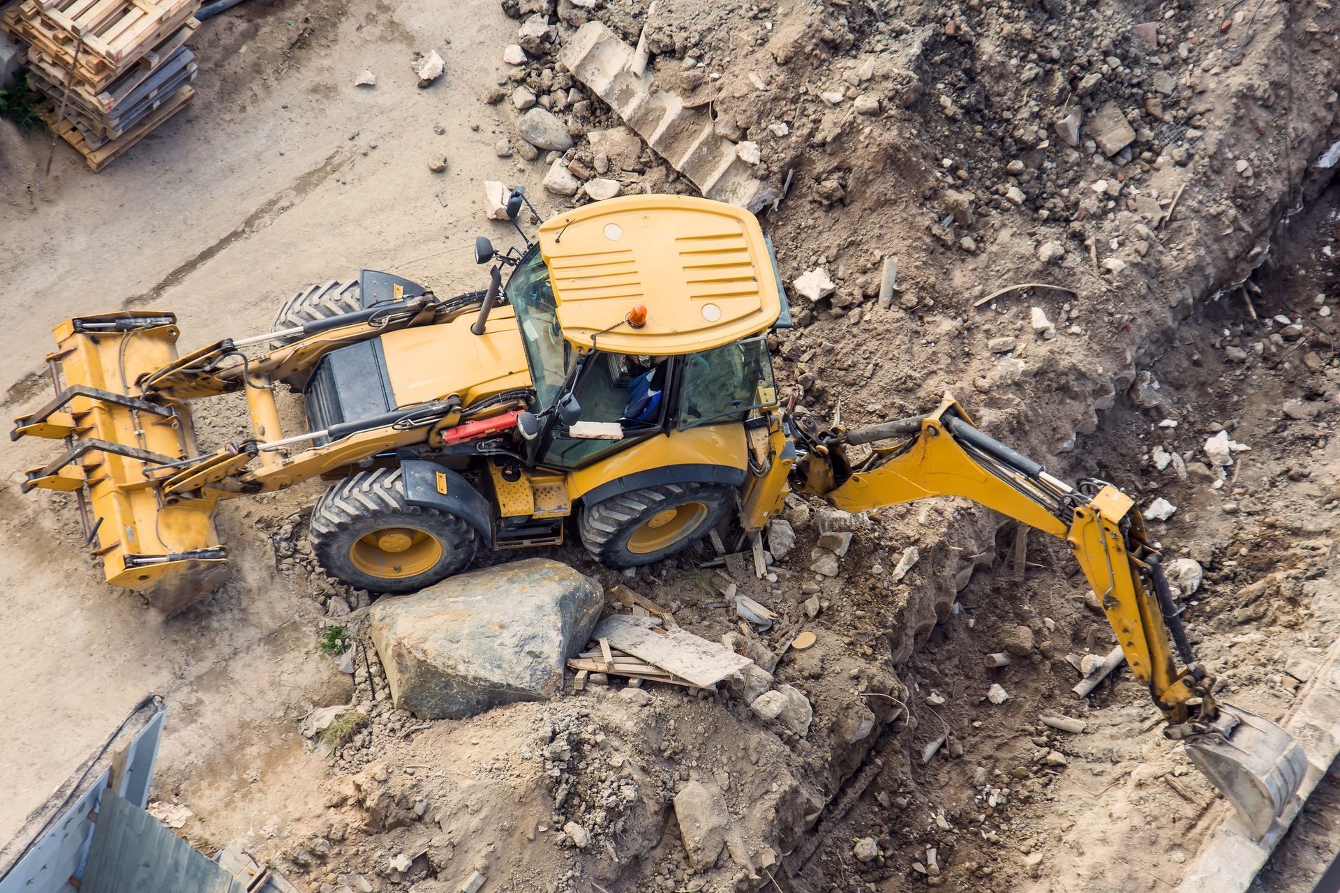 Yellow backhoe digging in a construction site, top view.
