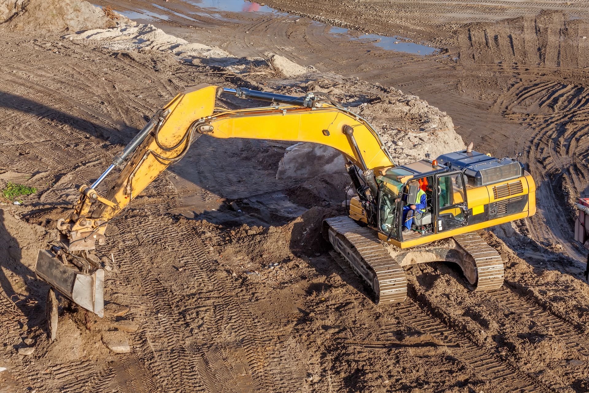 Yellow excavator digging in a muddy construction site.