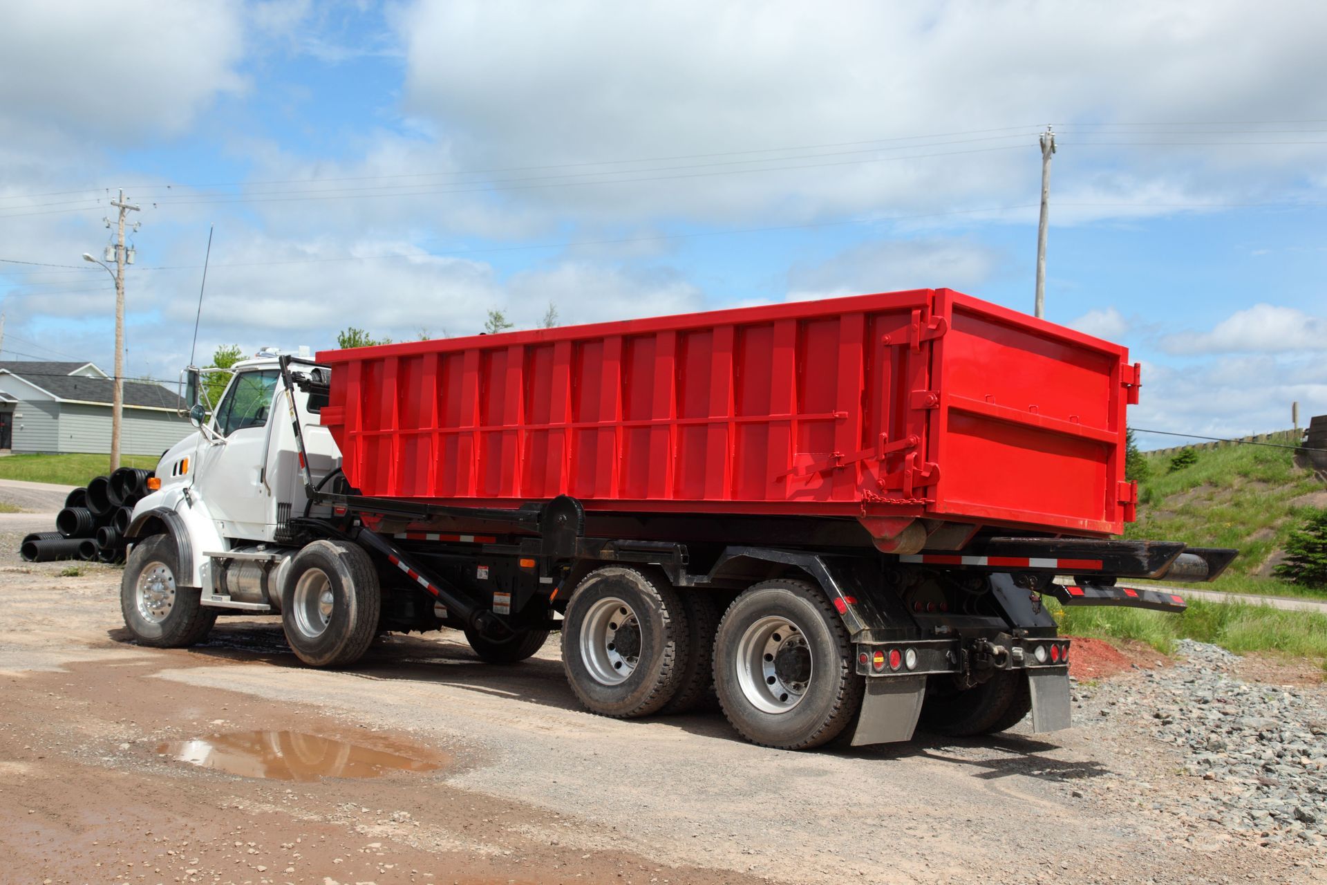 Red dump truck on a gravel road against a blue sky.