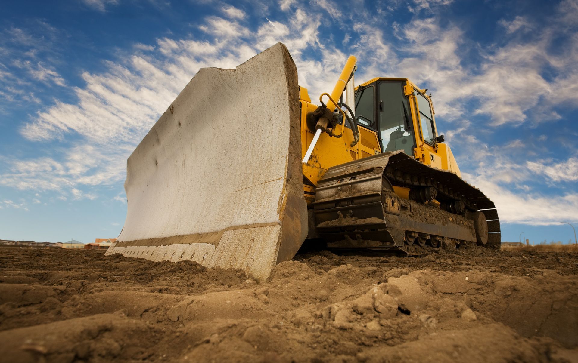 Yellow bulldozer pushing dirt across a construction site under a cloudy blue sky.