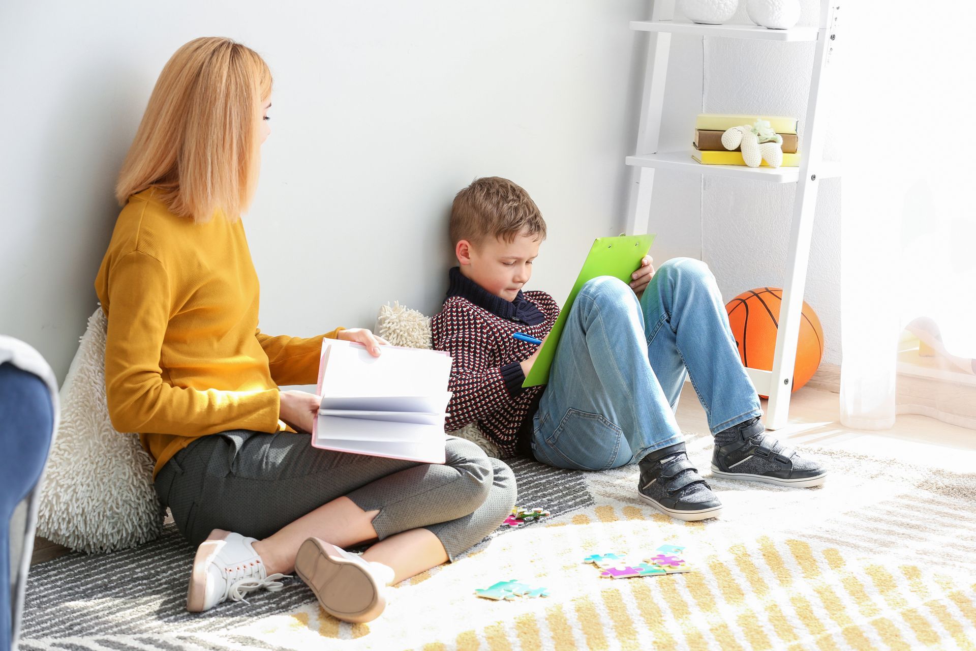 Boy painting a colorful rainbow on a window, squatting indoors with paint supplies nearby.