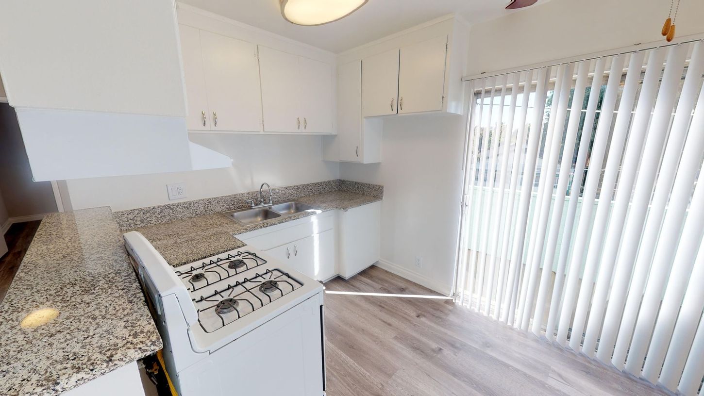 Kitchen with white cabinets, speckled countertops, stove, and sliding glass door with blinds.