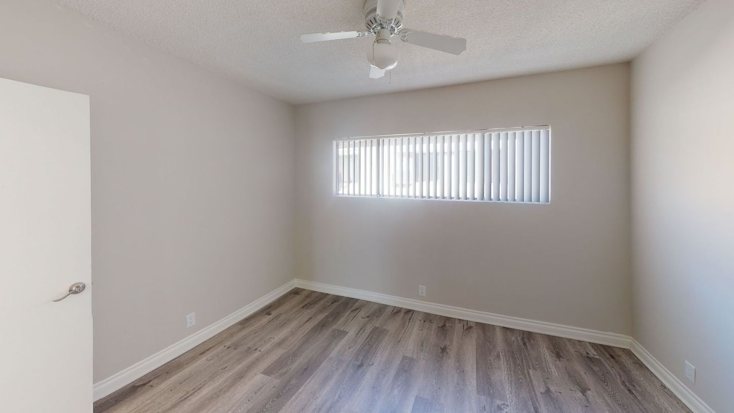 Empty bedroom with gray walls, wood-look flooring, and a window with blinds.
