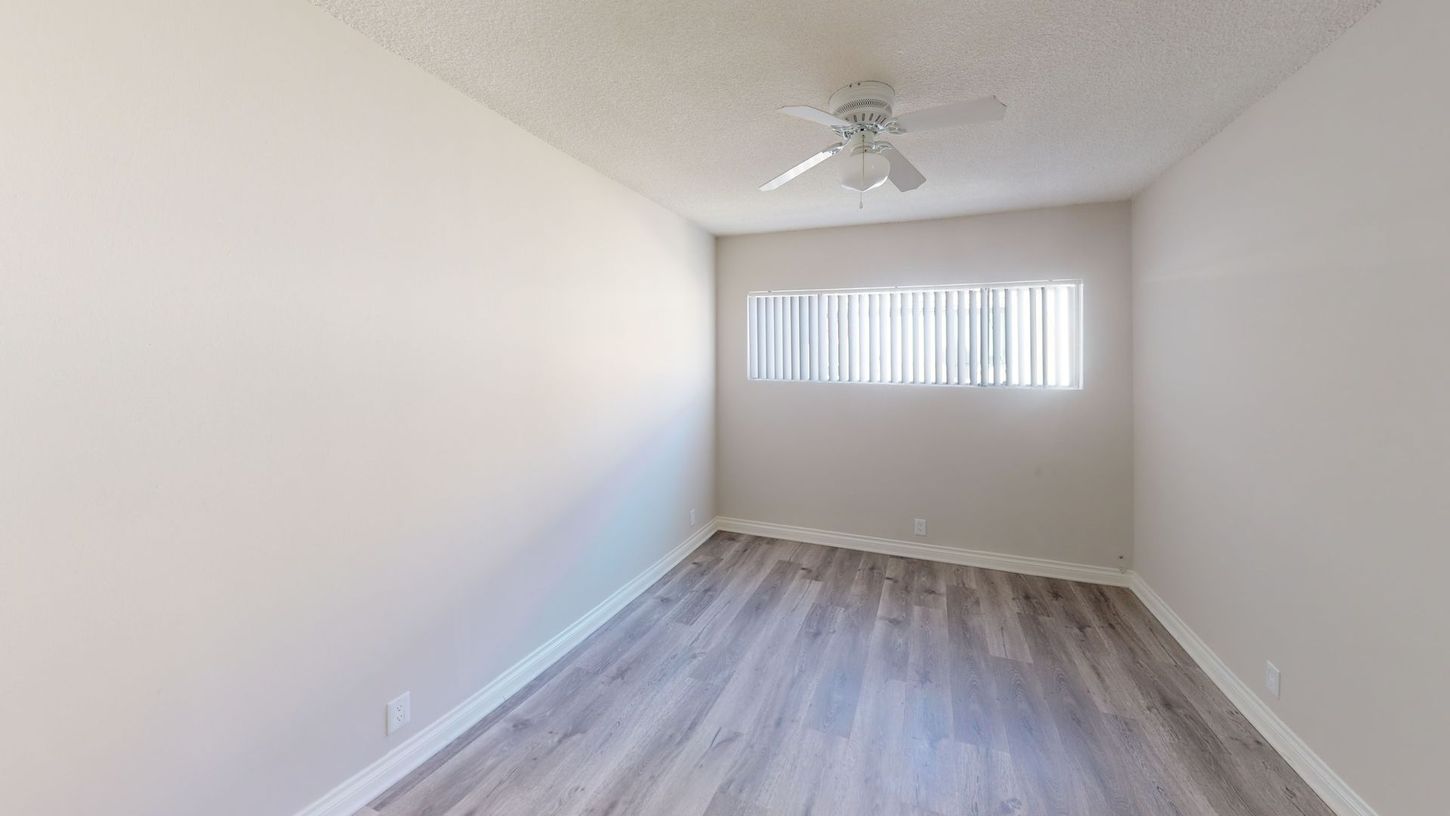 Empty room with gray laminate flooring, white walls, and a window with blinds.