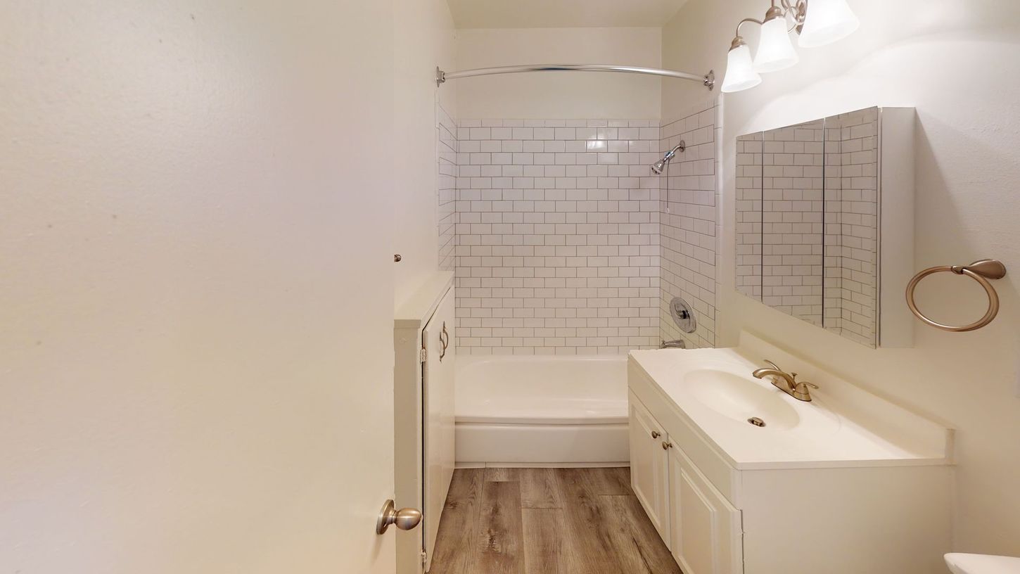 Bathroom with white fixtures, subway tile, and wood-look flooring.