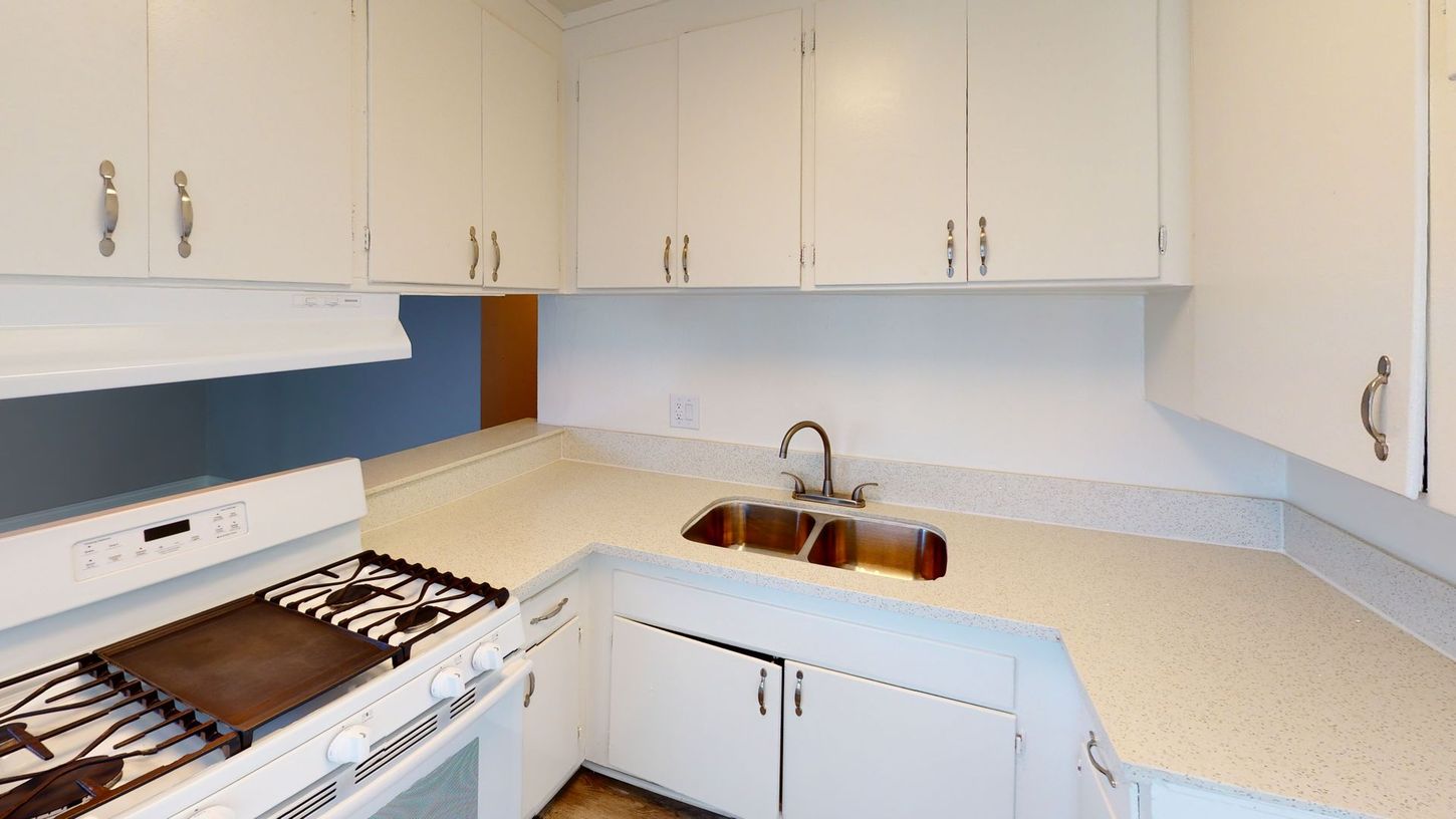 White kitchen with white cabinets, light countertops, and a stove.