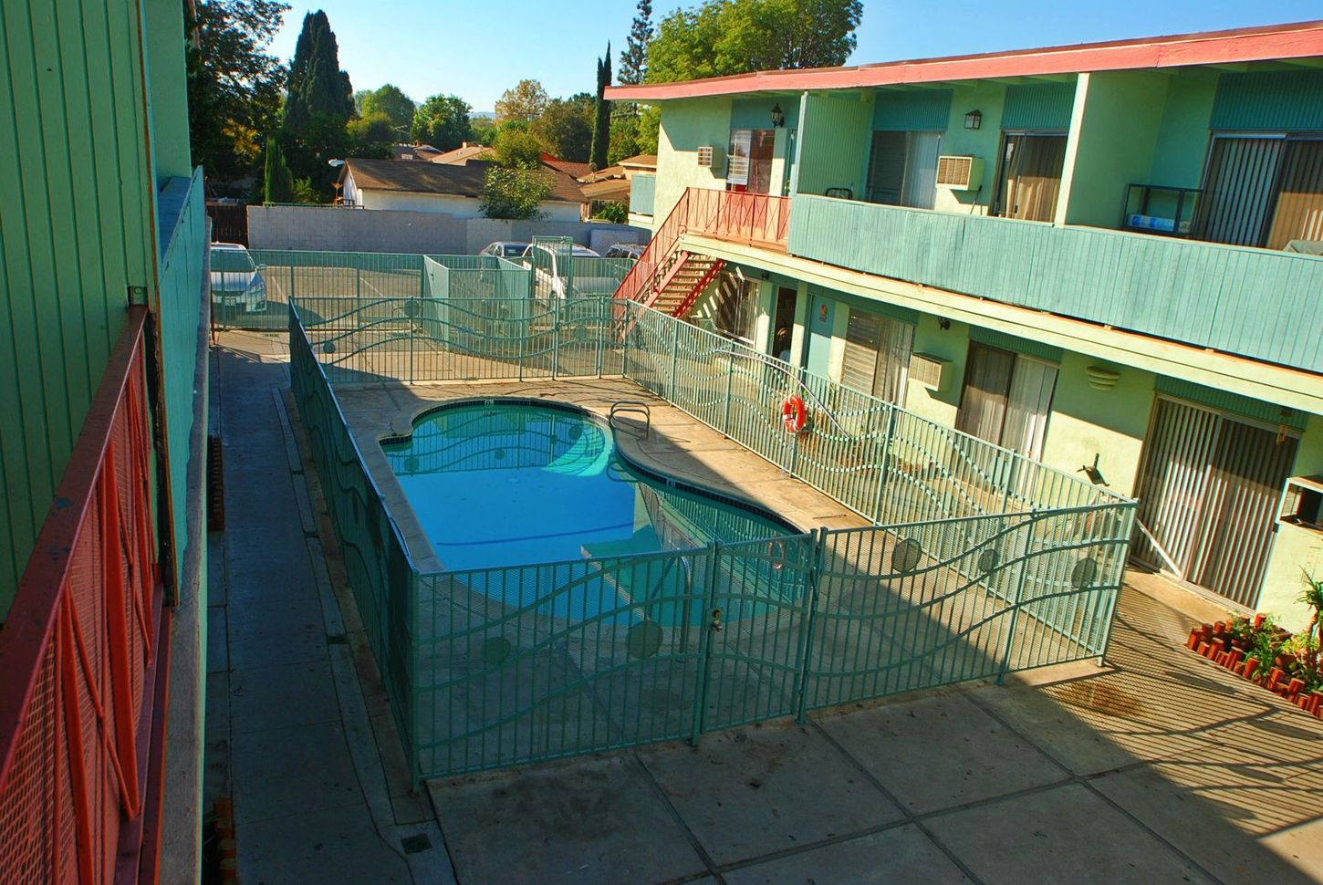 Courtyard with turquoise-painted apartments, a small pool, and matching decorative fencing.