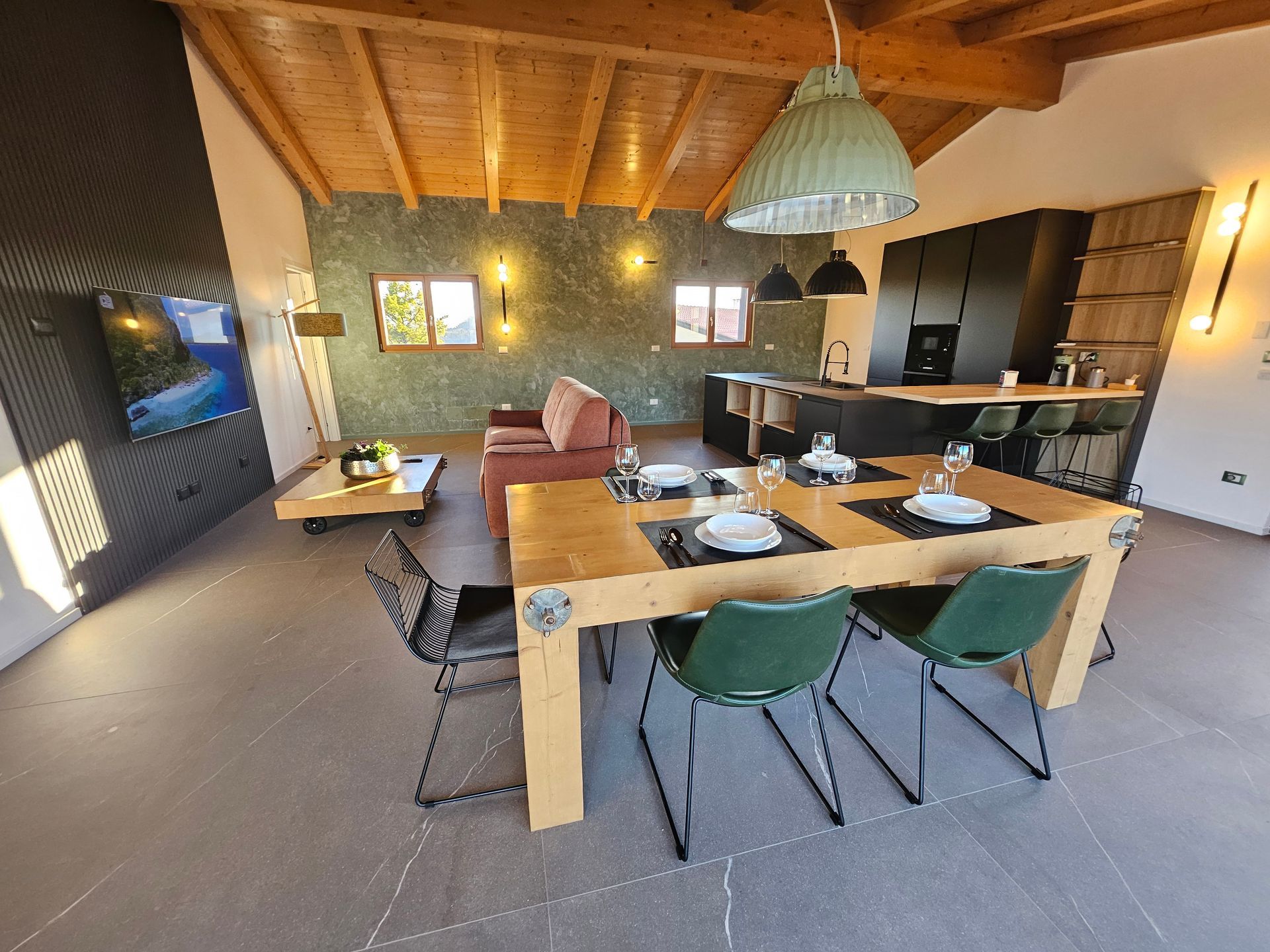 Accogliente interno del ristorante con tavoli in legno, sedie verdi, lampade a sospensione e un bancone bar.