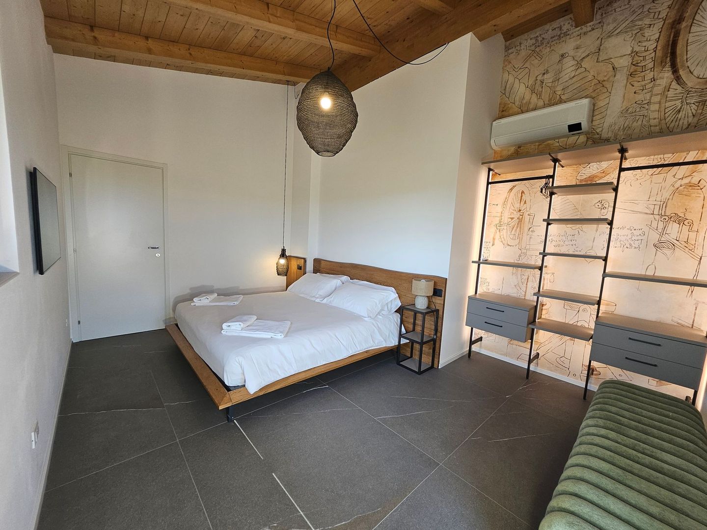 Camera da letto minimalista con soffitto in legno, letto, lampada a sospensione, mensole e divano-panca.