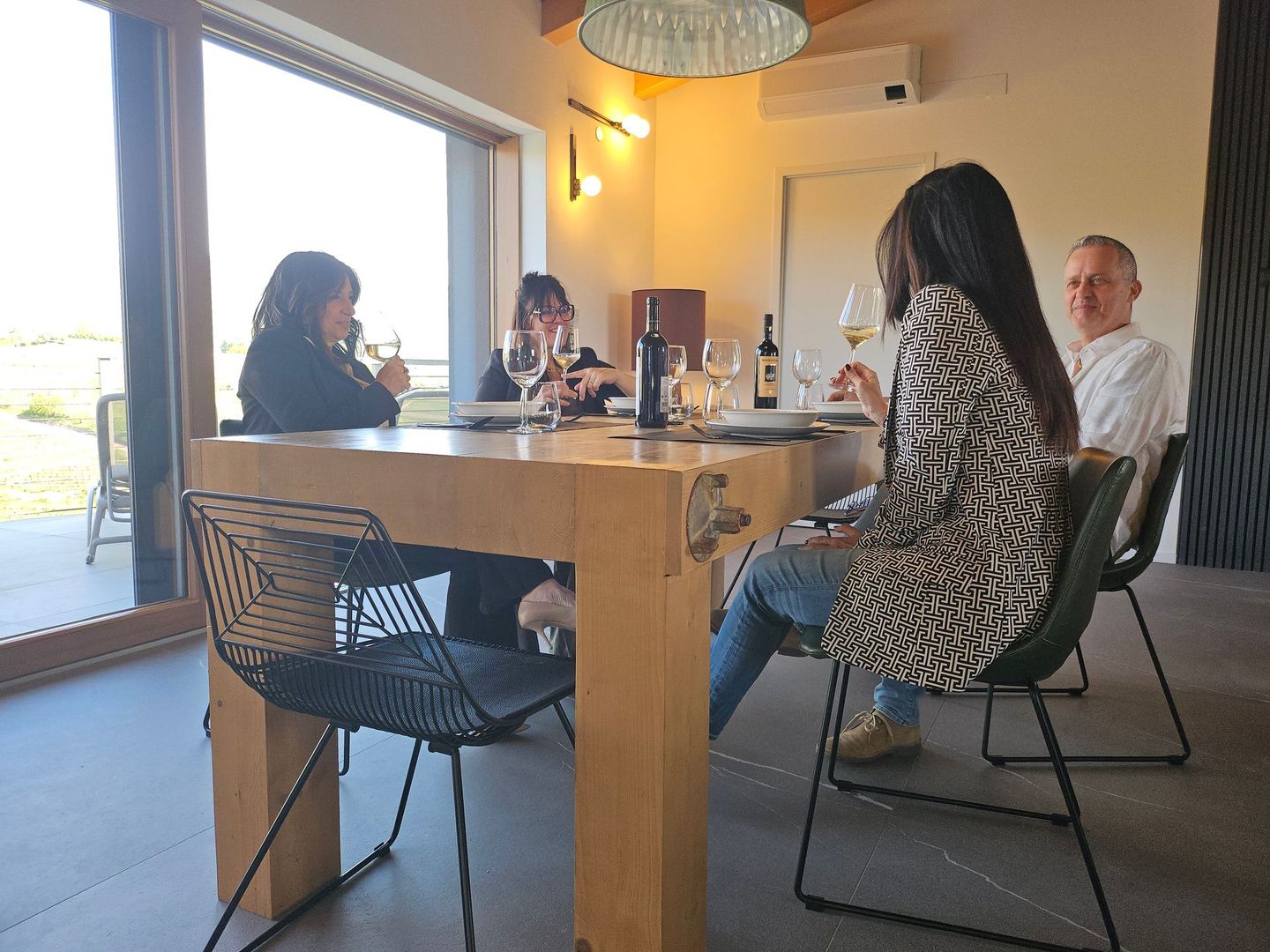 In una stanza luminosa, alcune persone erano sedute attorno a un tavolo di legno e conversavano vicino a una grande porta aperta.