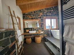 Bagno rustico con pareti in pietra, vasca freestanding, mobile lavabo doppio e sgabelli intrecciati.