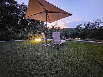 Il prato del cortile al crepuscolo con un ombrellone da patio, una sedia a sdraio e luci da giardino soffuse.