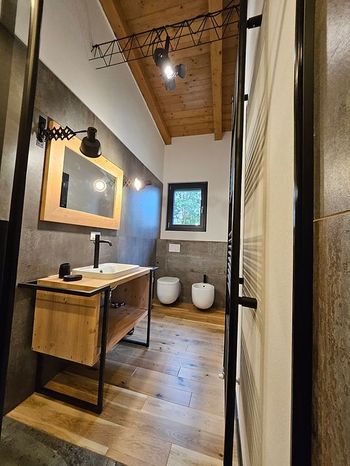 Bagno moderno con mobile lavabo in legno, specchio a parete, vasca freestanding e soffitto in legno illuminato da un lucernario.