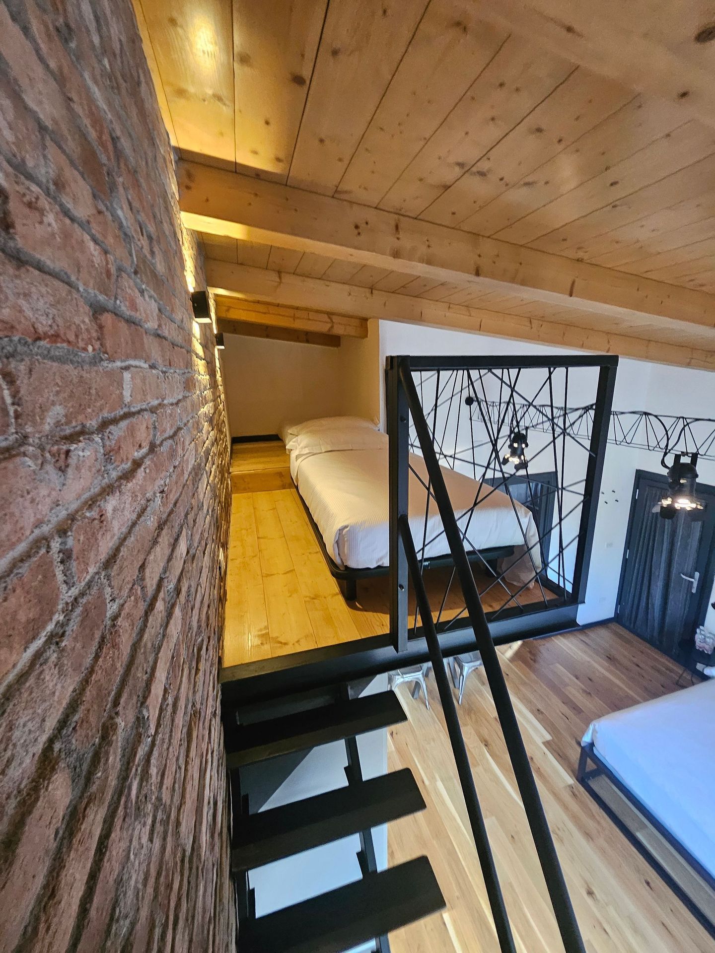 Camera da letto soppalcata con pareti in legno, letti a castello e scala in metallo nero all'interno di una baita rustica.