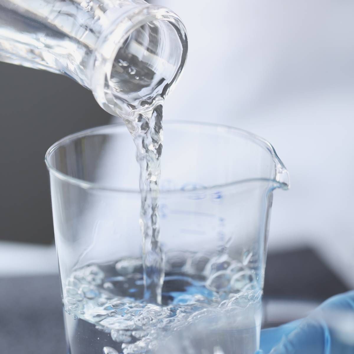 Clear liquid being poured from a bottle into a beaker in a lab setting.
