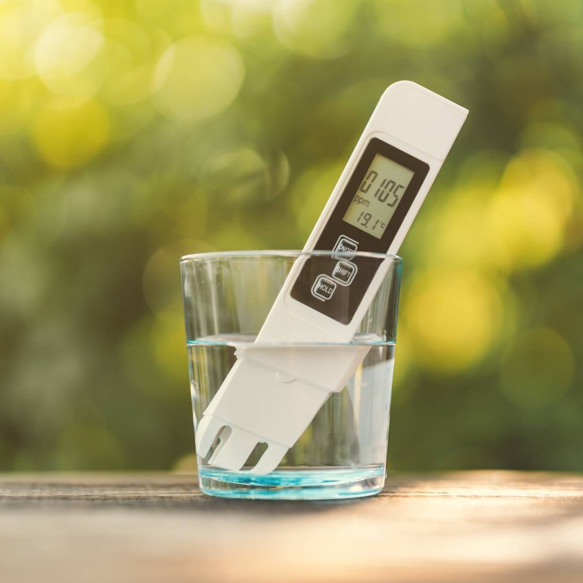 A white TDS meter submerged in a glass of water; shows the water's purity outdoors.