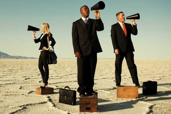 Three people in suits using megaphones on boxes in a desert.