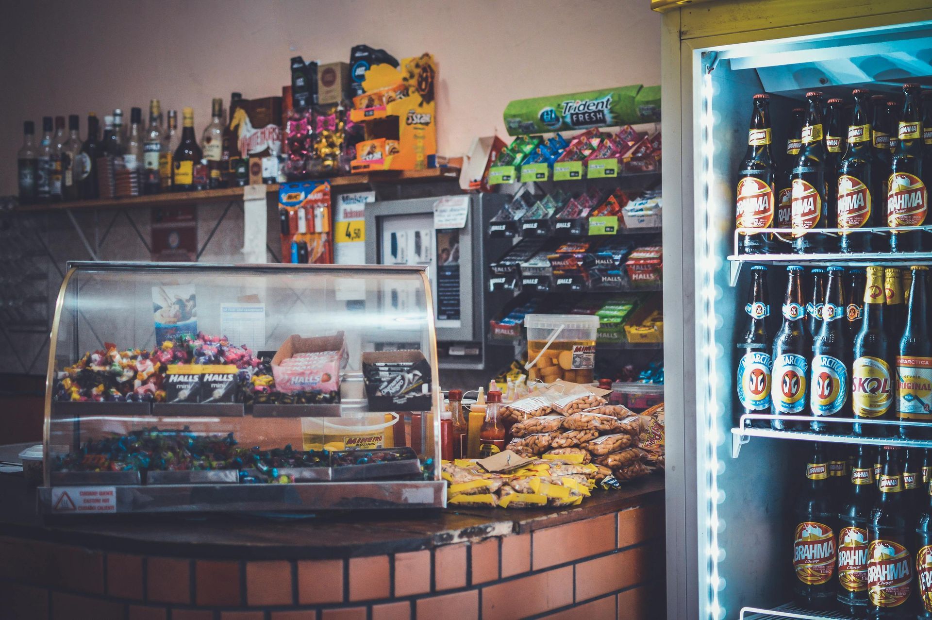 A convenience store interior with snacks, drinks in a cooler, and a display case of sweets on a counter.