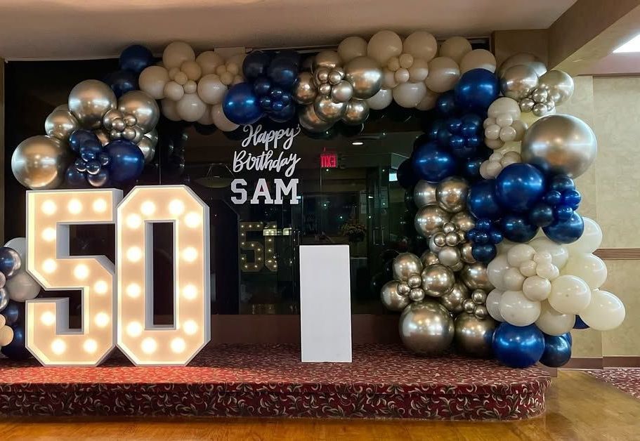 A large number 50 is surrounded by balloons and lights.