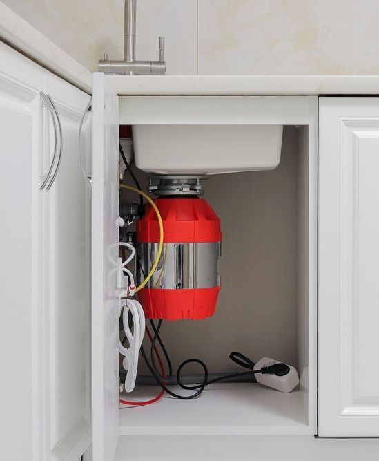 A red garbage disposal is sitting under a sink in a kitchen.