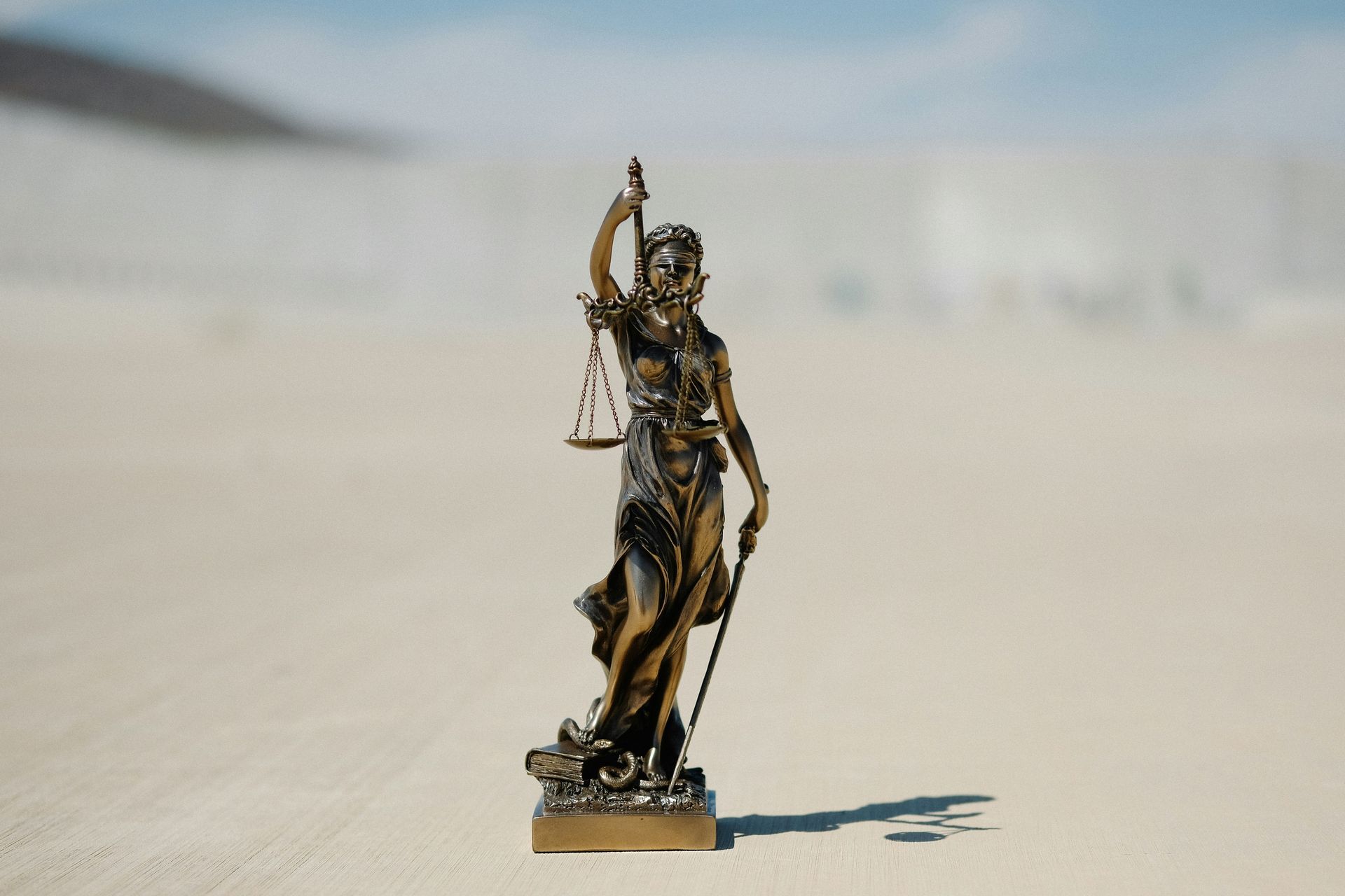 Statue of Lady Justice holding scales and sword, set outdoors.