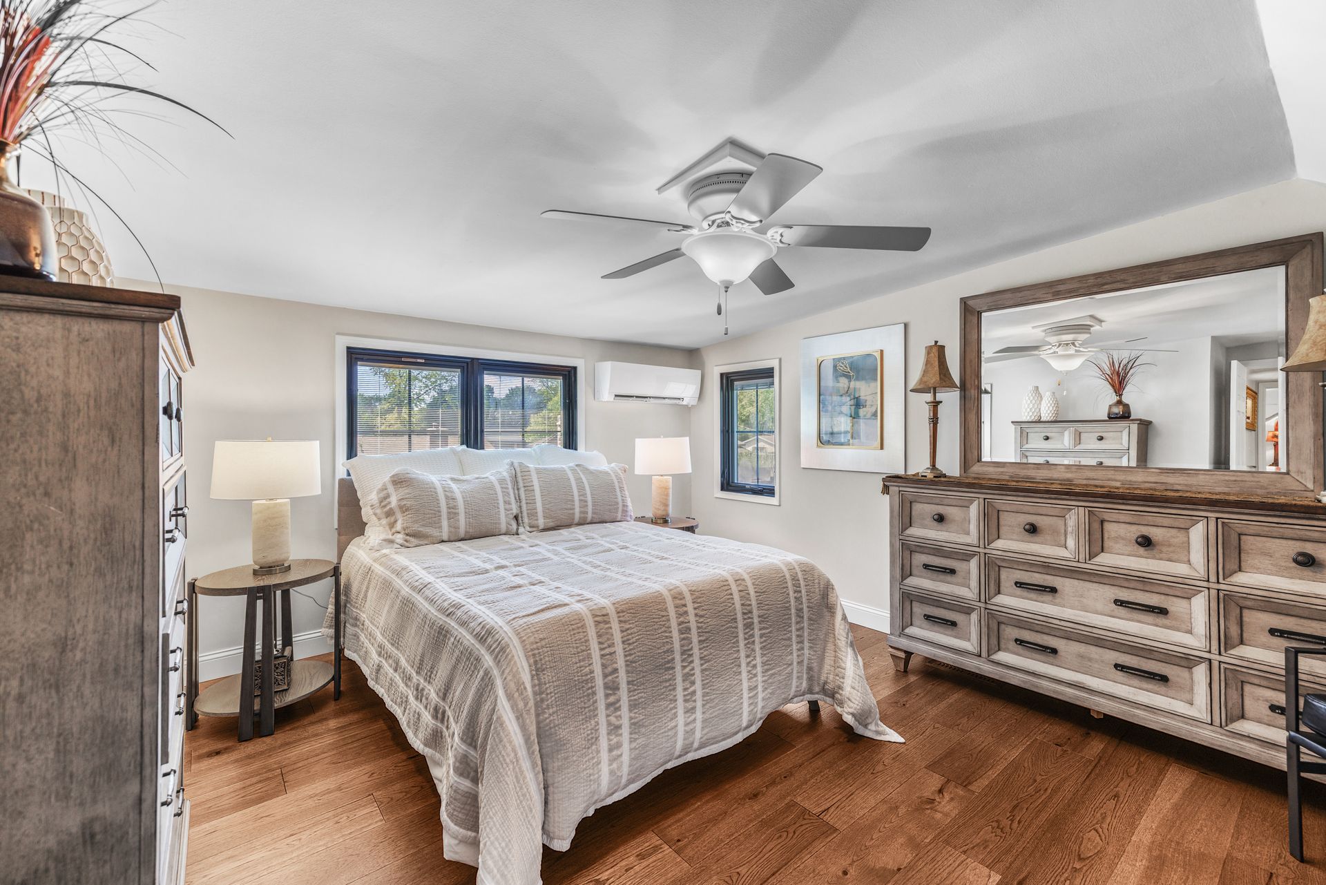 Bedroom with a bed, dresser with a mirror, nightstand, and ceiling fan. Wooden floors and neutral color scheme.